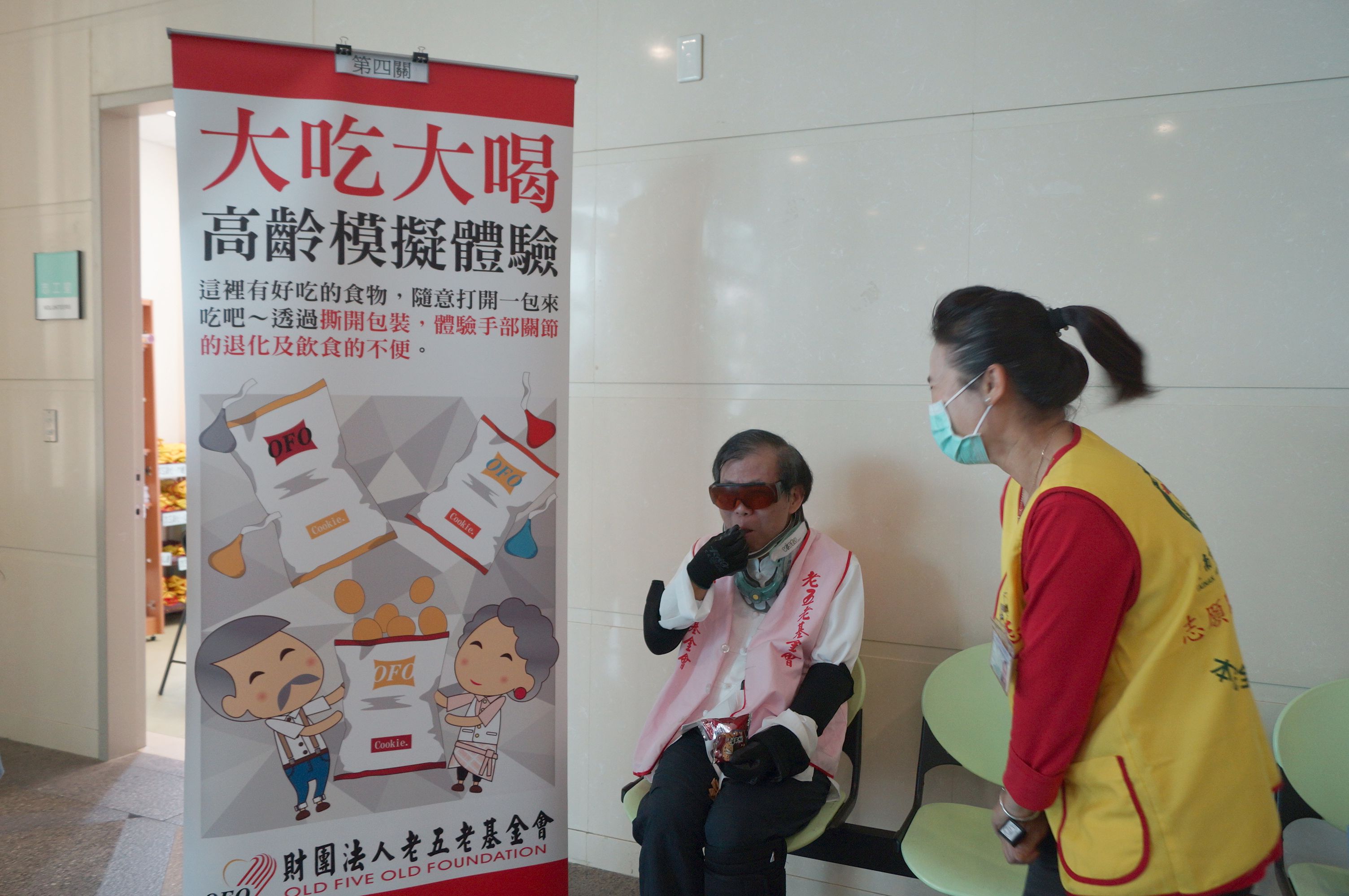 吳彬安副院長模擬體驗高齡者撕開包裝食物吃東西。